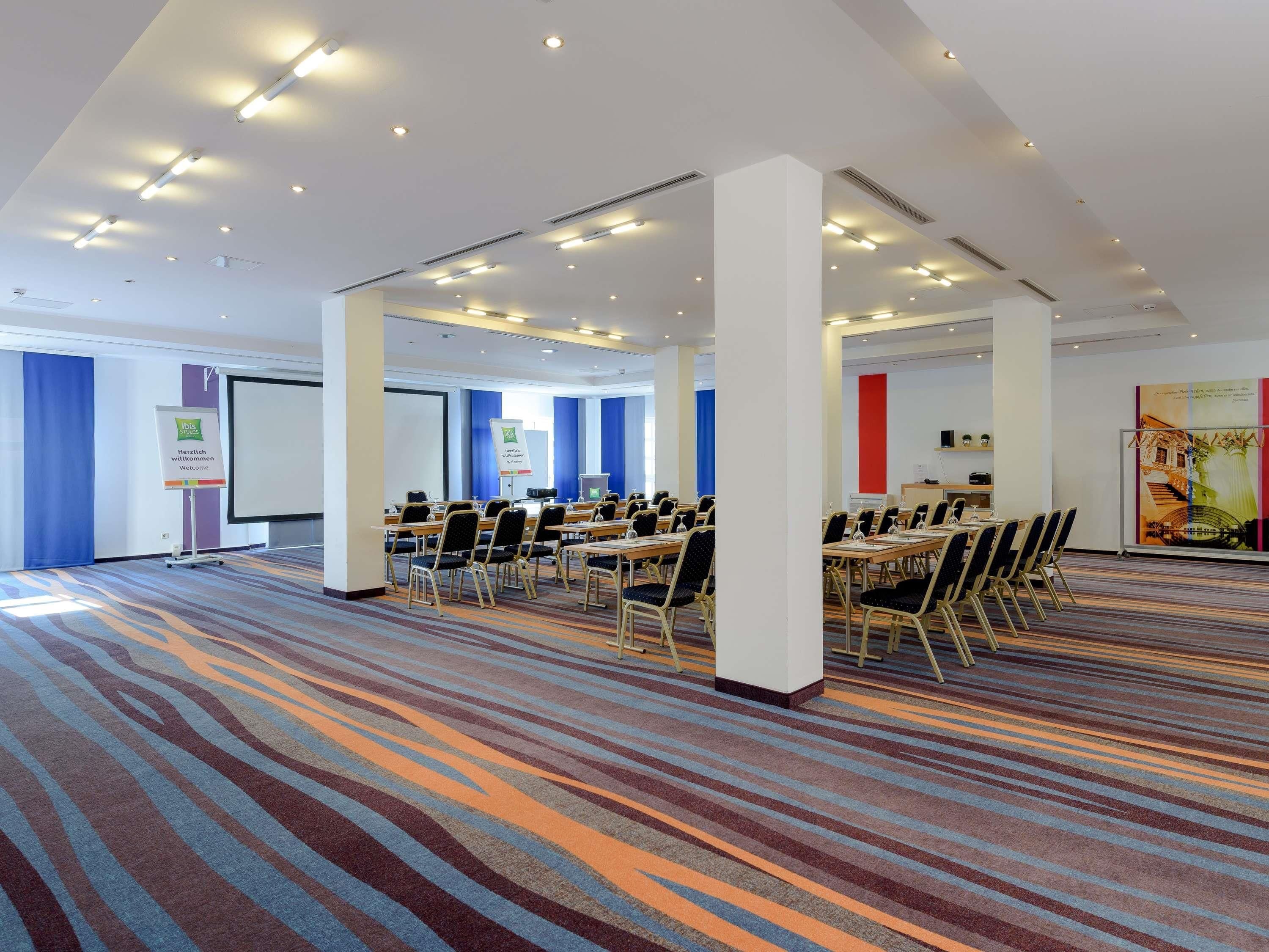 A conference room with tables and chairs, a projector screen, and a banner.