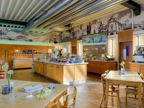 A modern kitchen with a central island, wooden cabinets, and a mural of cityscapes on the wall. - ibis Styles Leipzig (Schkeuditz)