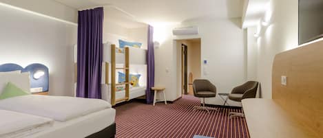 A hotel room with a bed, a desk, a chair, a small table, and a wardrobe.