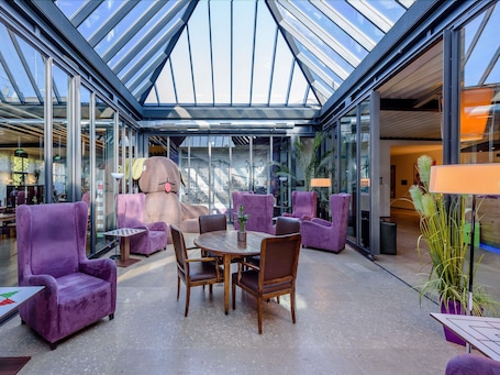 Un intérieur moderne avec un plafond en verre, des sièges violets et une grande statue de chien.. ibis Styles Leipzig