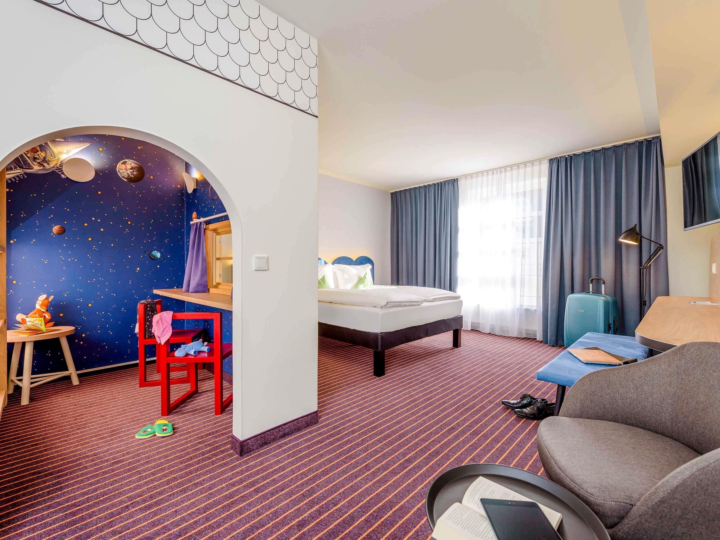 A hotel room with a bed, a desk, a chair, a sofa, and a starry wall design.