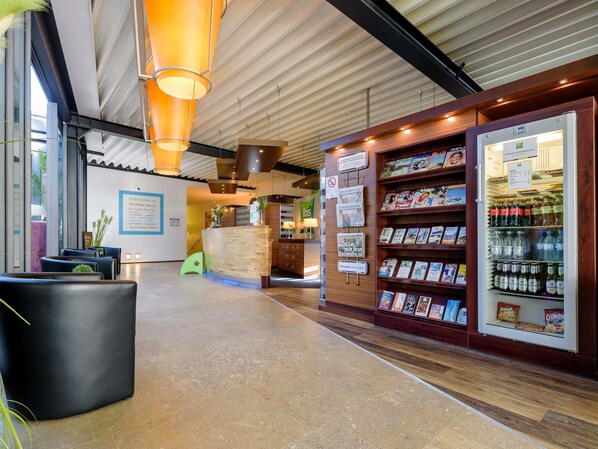 Un espace d’accueil comprenant un comptoir de réception en bois, un présentoir à magazines et un réfrigérateur pour les boissons.