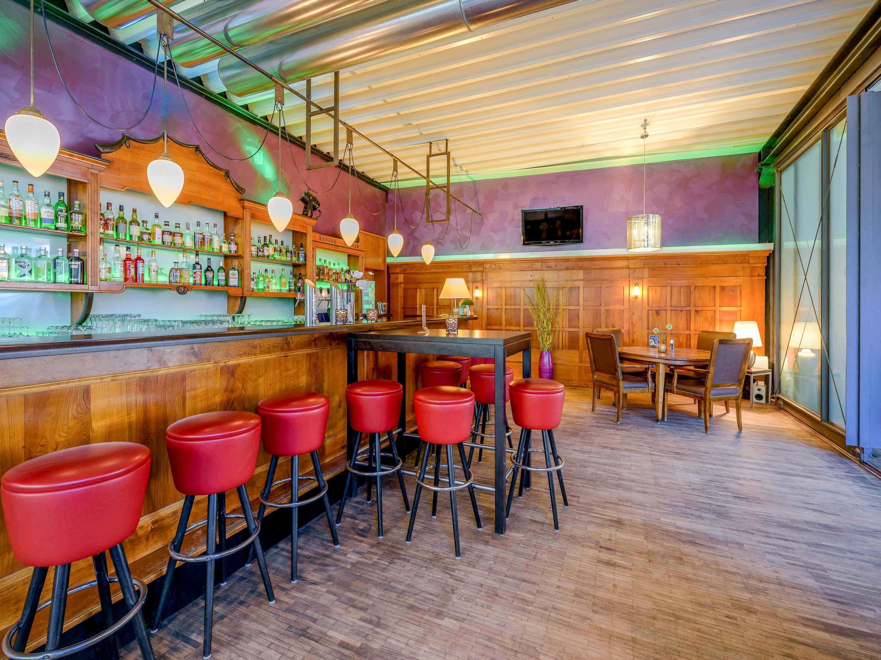 Zona de bar con mostradores de madera, taburetes rojos y una variedad de botellas y vasos.