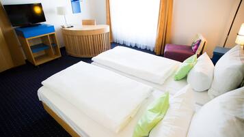 Ein Hotelzimmer mit zwei Betten, einem Schreibtisch, einem Fernseher und einem kleinen runden Tisch.