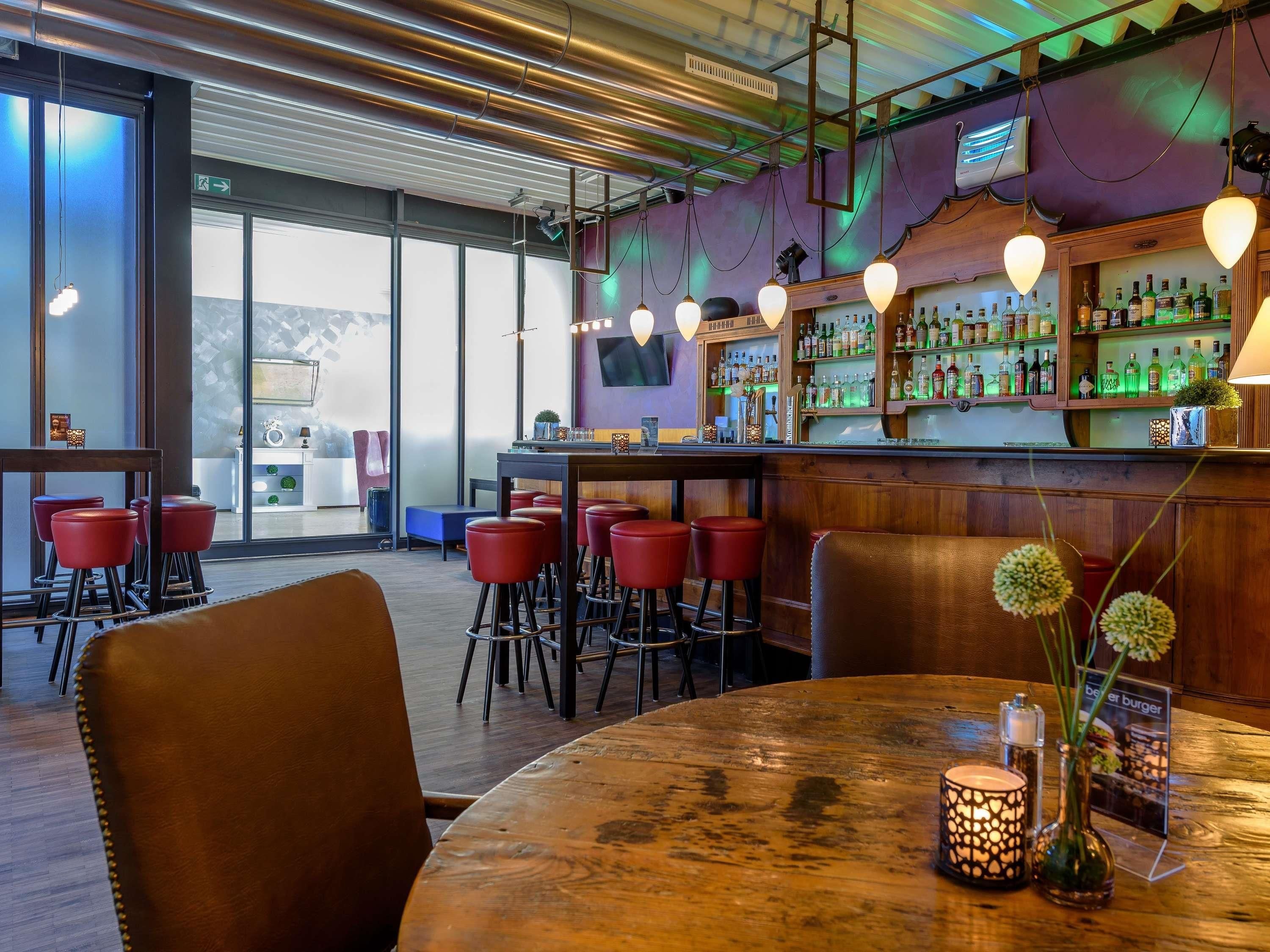 A bar area with wooden tables and red bar stools, a bar counter with bottles, and a large window with a view.