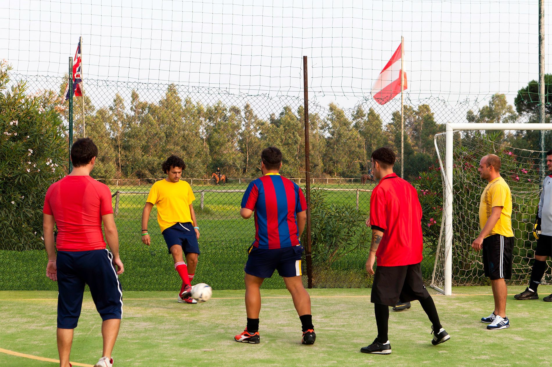Un campo da calcio con giocatori con maglie di diversi colori, un portiere e una bandiera.