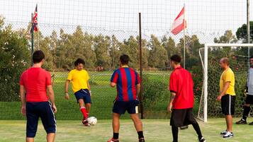 Un campo da calcio con giocatori con maglie di diversi colori, un portiere e una bandiera.