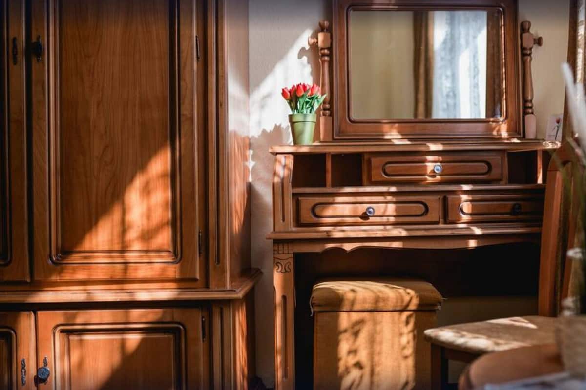 A wooden dresser with a mirror, a small stool, and a vase with flowers.