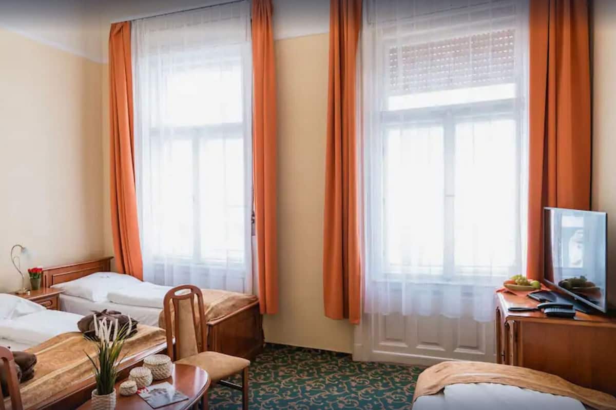 A hotel room with two beds, a desk, a chair, a television, and a window with curtains.