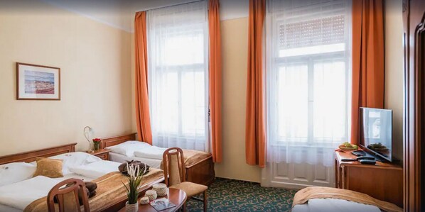 Habitación de hotel con dos camas, un escritorio, una silla, un televisor y una ventana con cortinas.