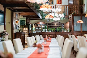 A long dining table with white chairs, a red table runner, and hanging lamps. - Hotel Unio Budapest (Budapest)