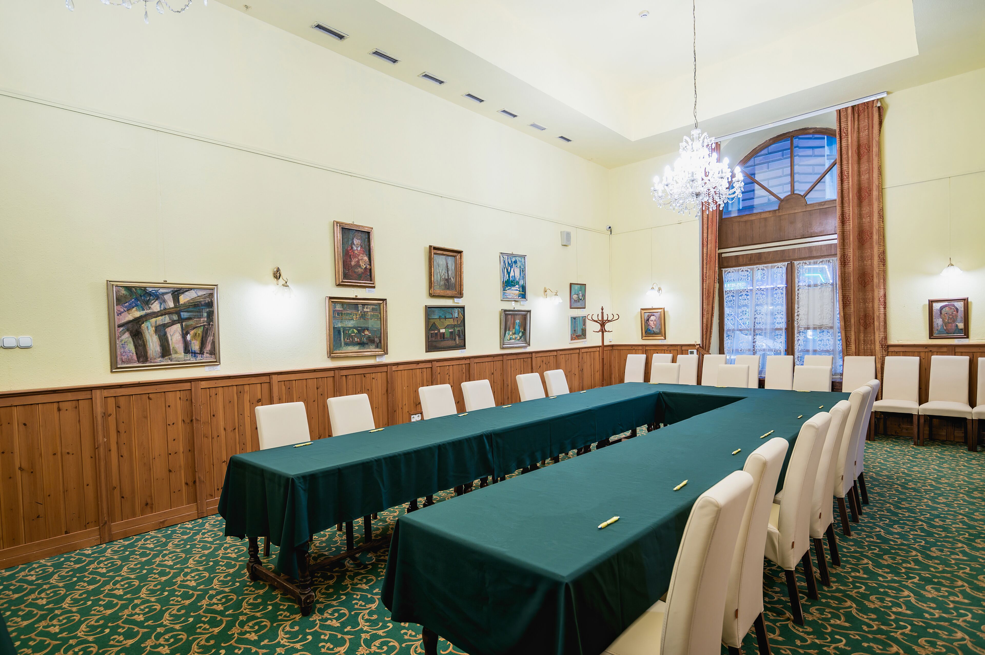 A conference room with a long table, white chairs, wooden paneling, and framed artwork on the walls.