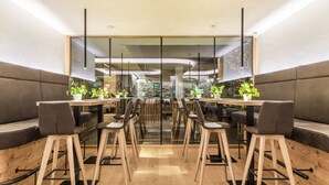 A modern dining area with wooden tables and chairs, glass partitions, and potted plants. - Hotel Langgenhof (Brunico)