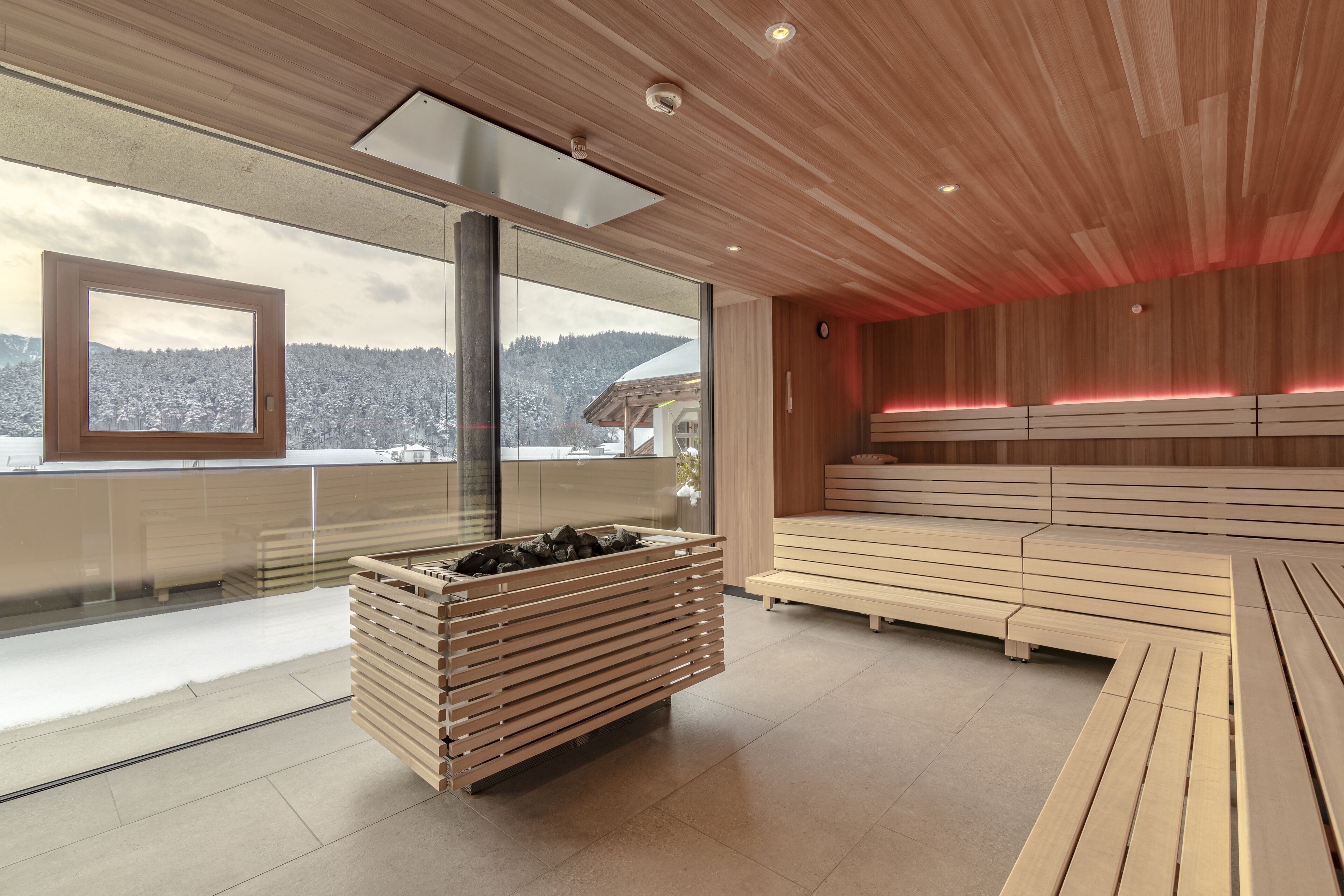Un espace de bien-être moderne doté d’un banc en bois, d’un bain en pierre chauffé et offrant une vue sur des montagnes enneigées.