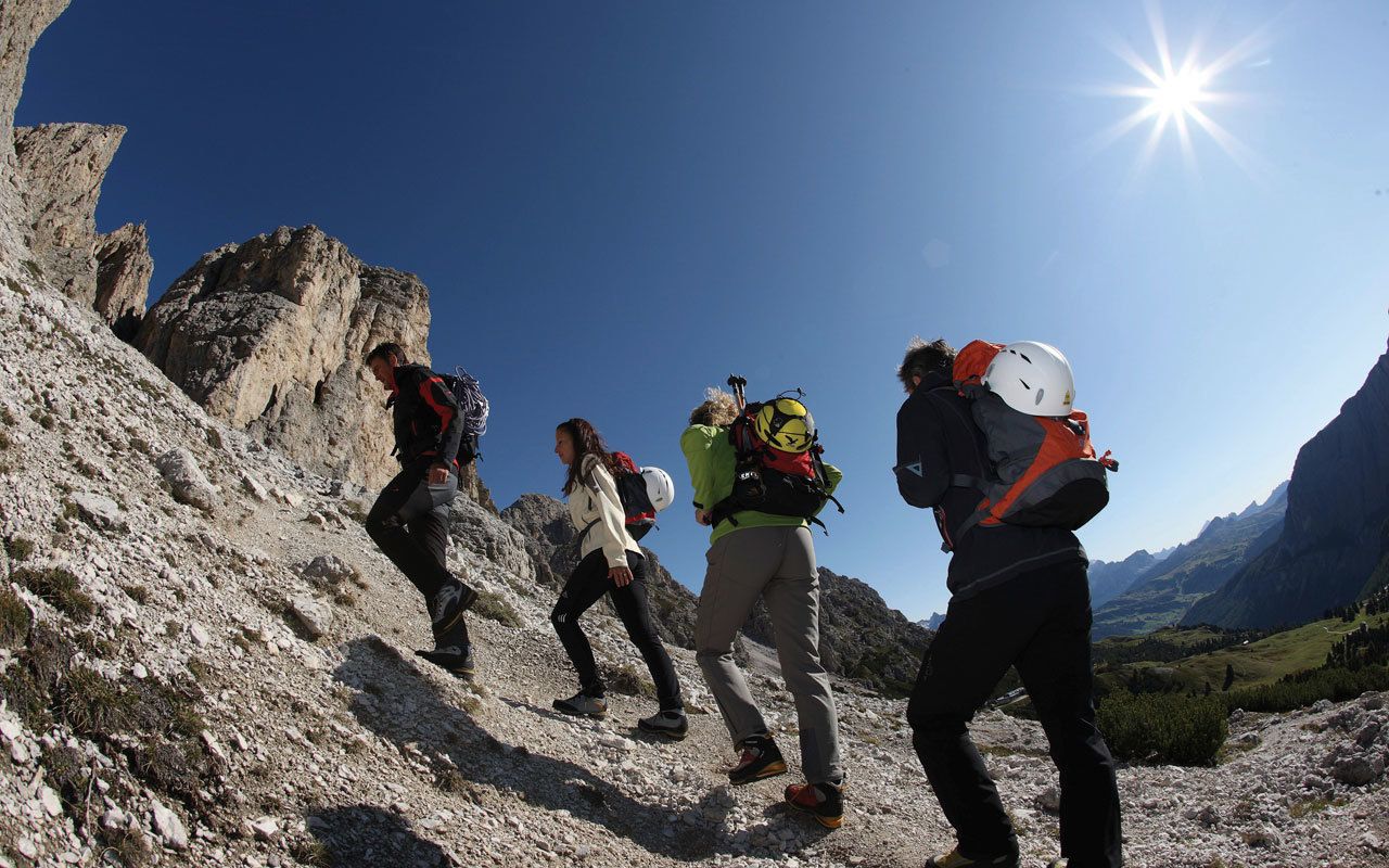A group of hikers on a rocky mountain trail with a clear sky.