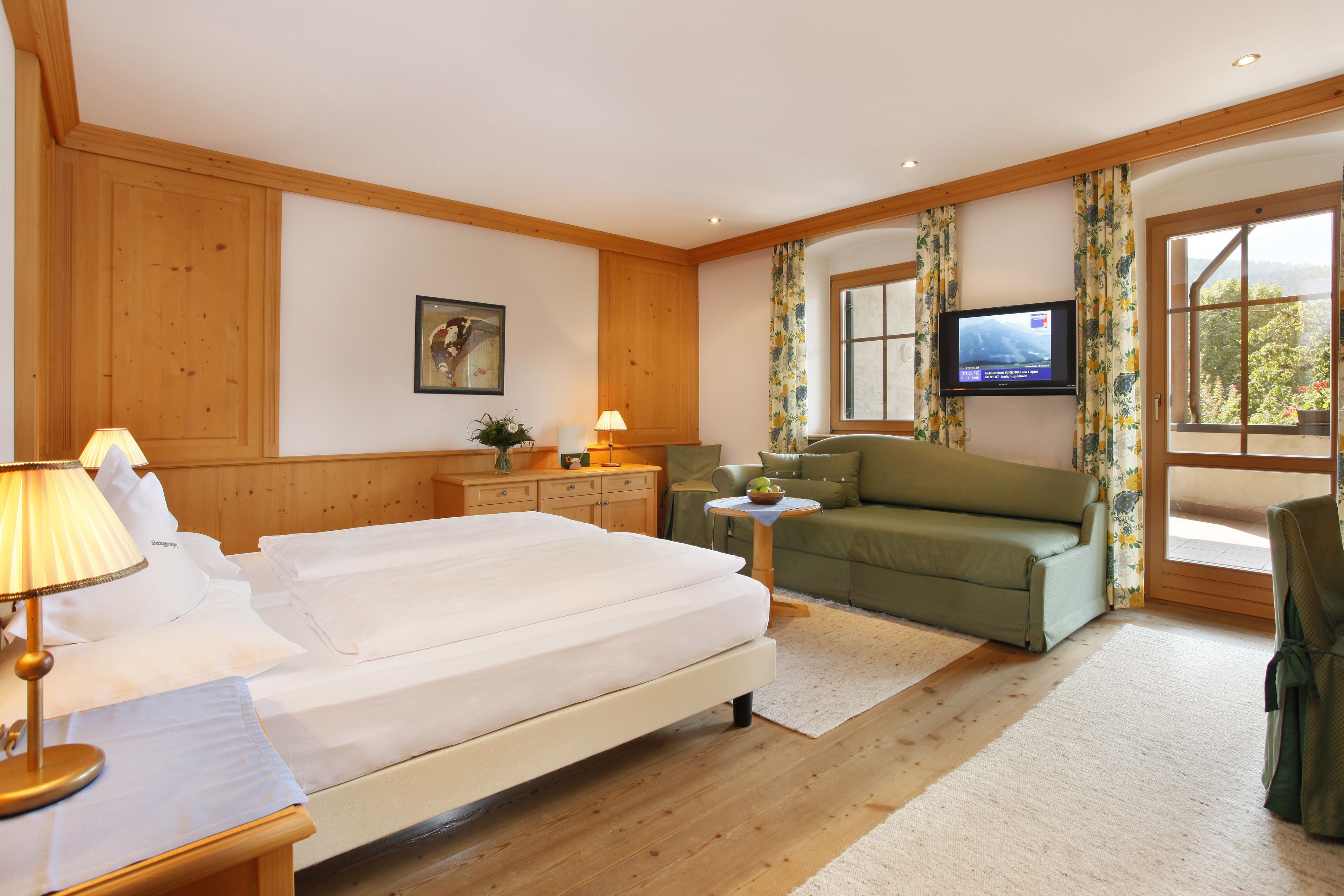 A hotel room with a bed, a sofa, a TV, and a window with curtains.