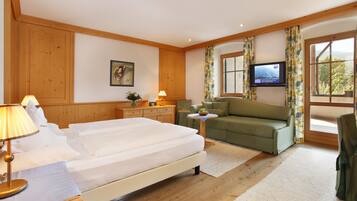 A hotel room with a bed, a sofa, a TV, and a window with curtains.