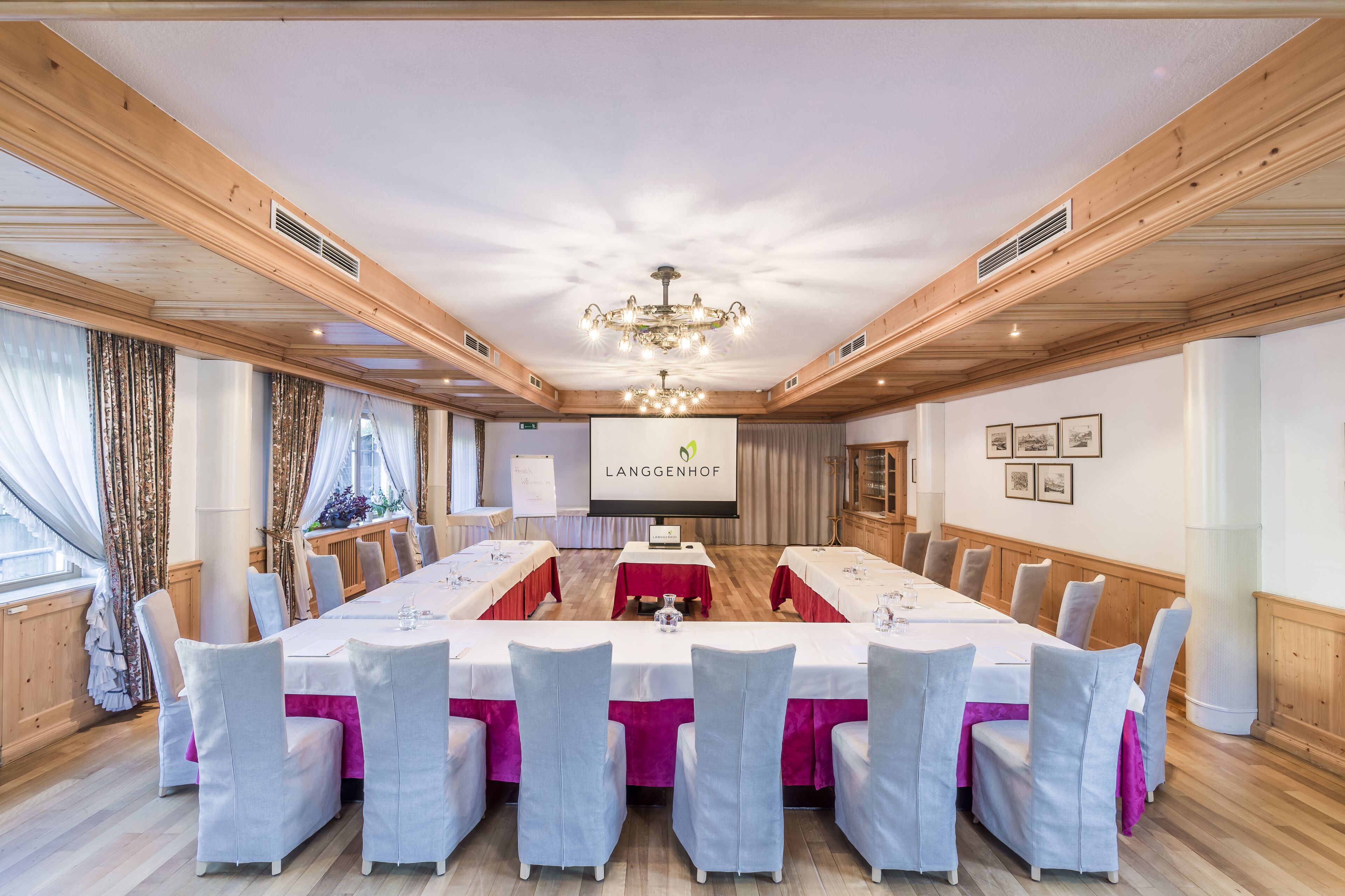 A conference room with a long table, white chairs, and a chandelier.