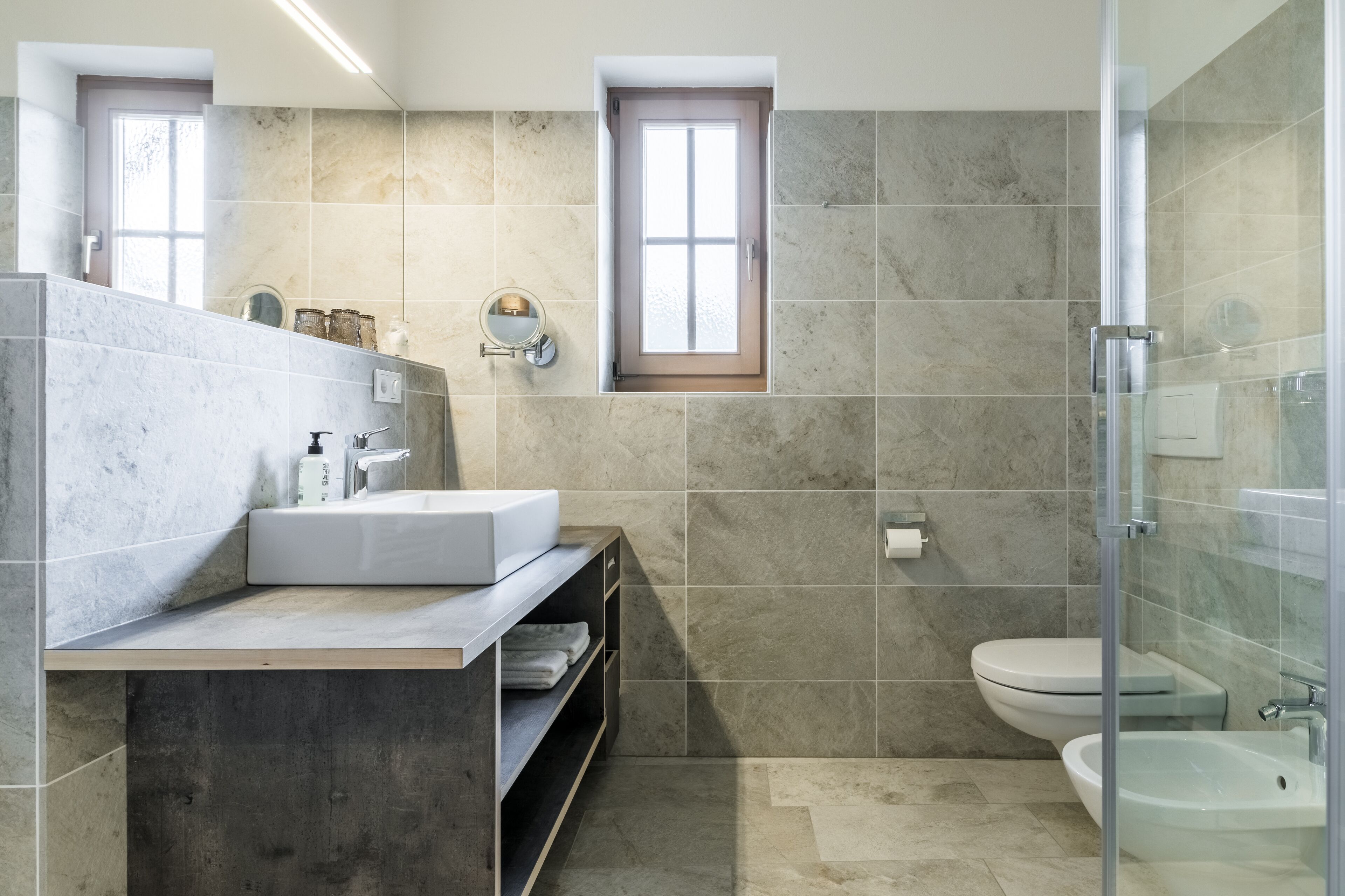 Un baño moderno con lavamanos de mármol, cabina de ducha de vidrio y un inodoro.