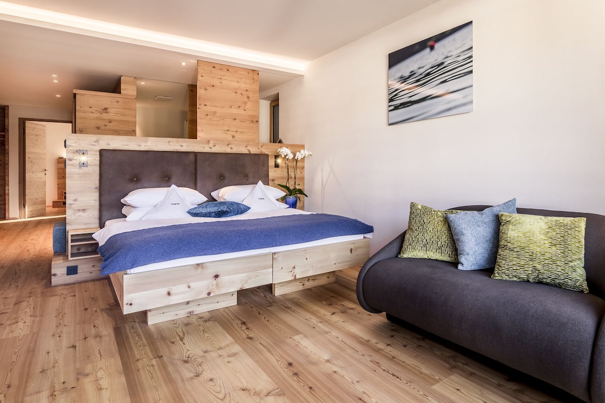 A bedroom with a wooden bed, a dark sofa, and a painting on the wall.