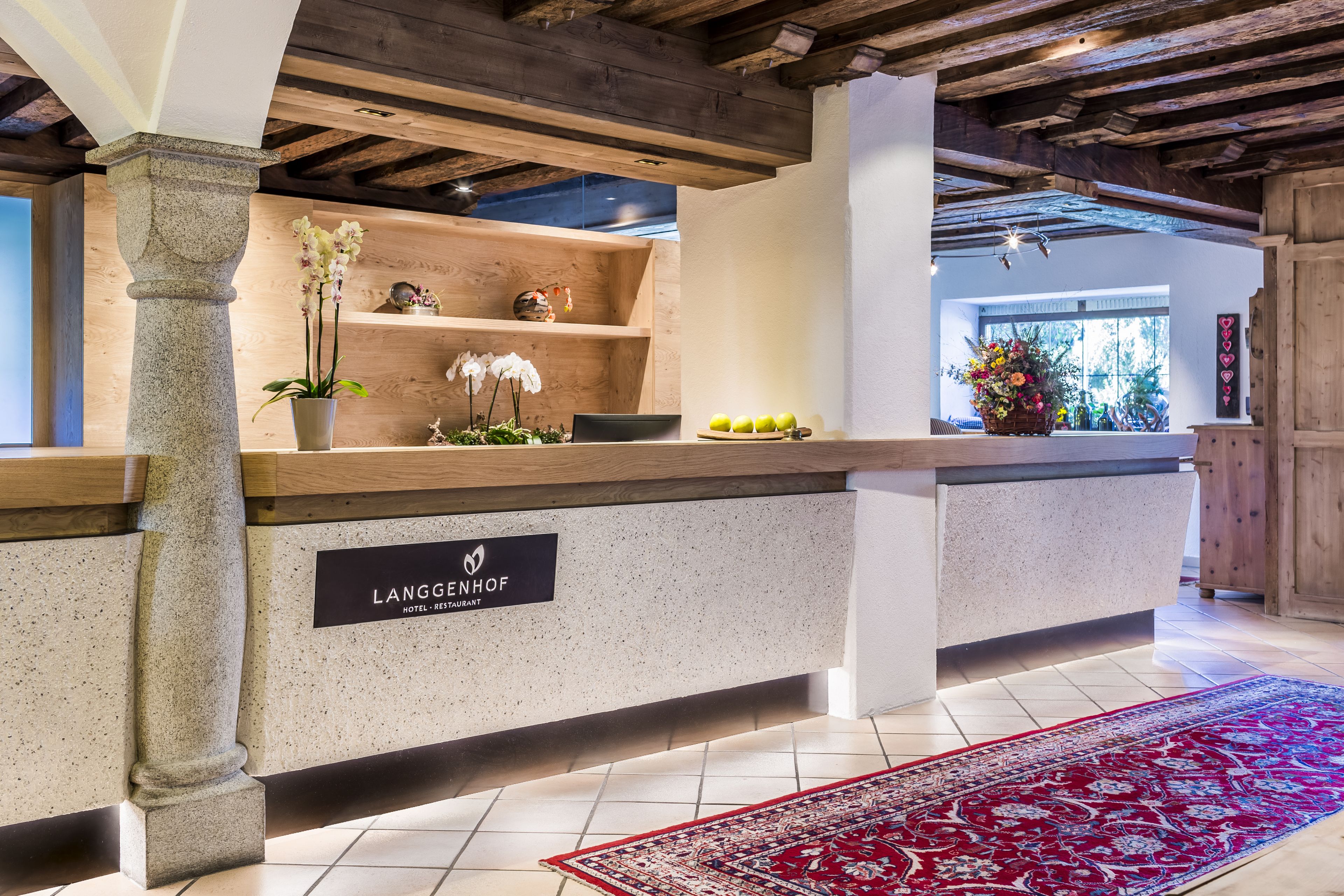 Uma área de recepção com um pilar de pedra, um balcão de madeira e uma placa com a inscrição "LANGGENHOF HOTEL RESTAURANT".