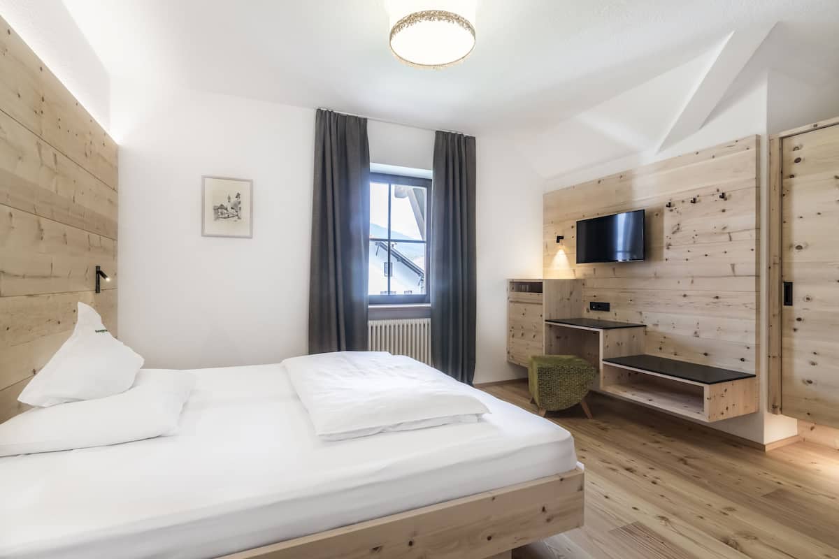 A modern bedroom with a wooden bed, a TV mounted on the wall, and a window with curtains.