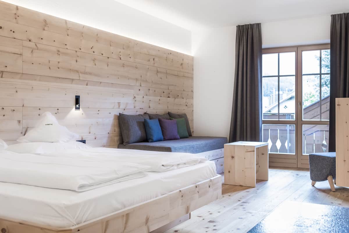 A modern bedroom with a wooden headboard, a bed with white linens, a gray sofa, and a small wooden table.