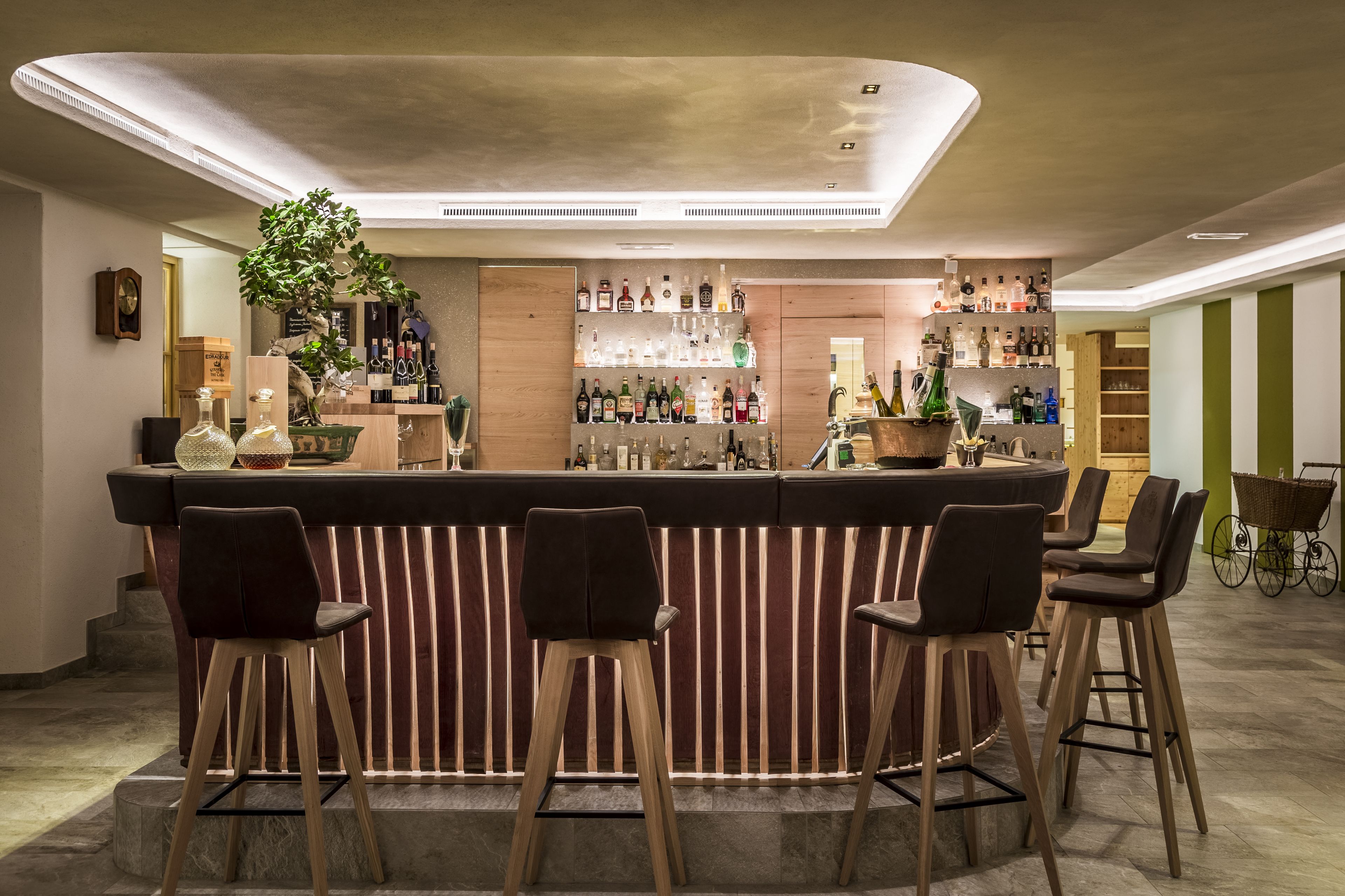 Una zona de bar con mostrador de madera, varios taburetes y una variedad de botellas y vasos.