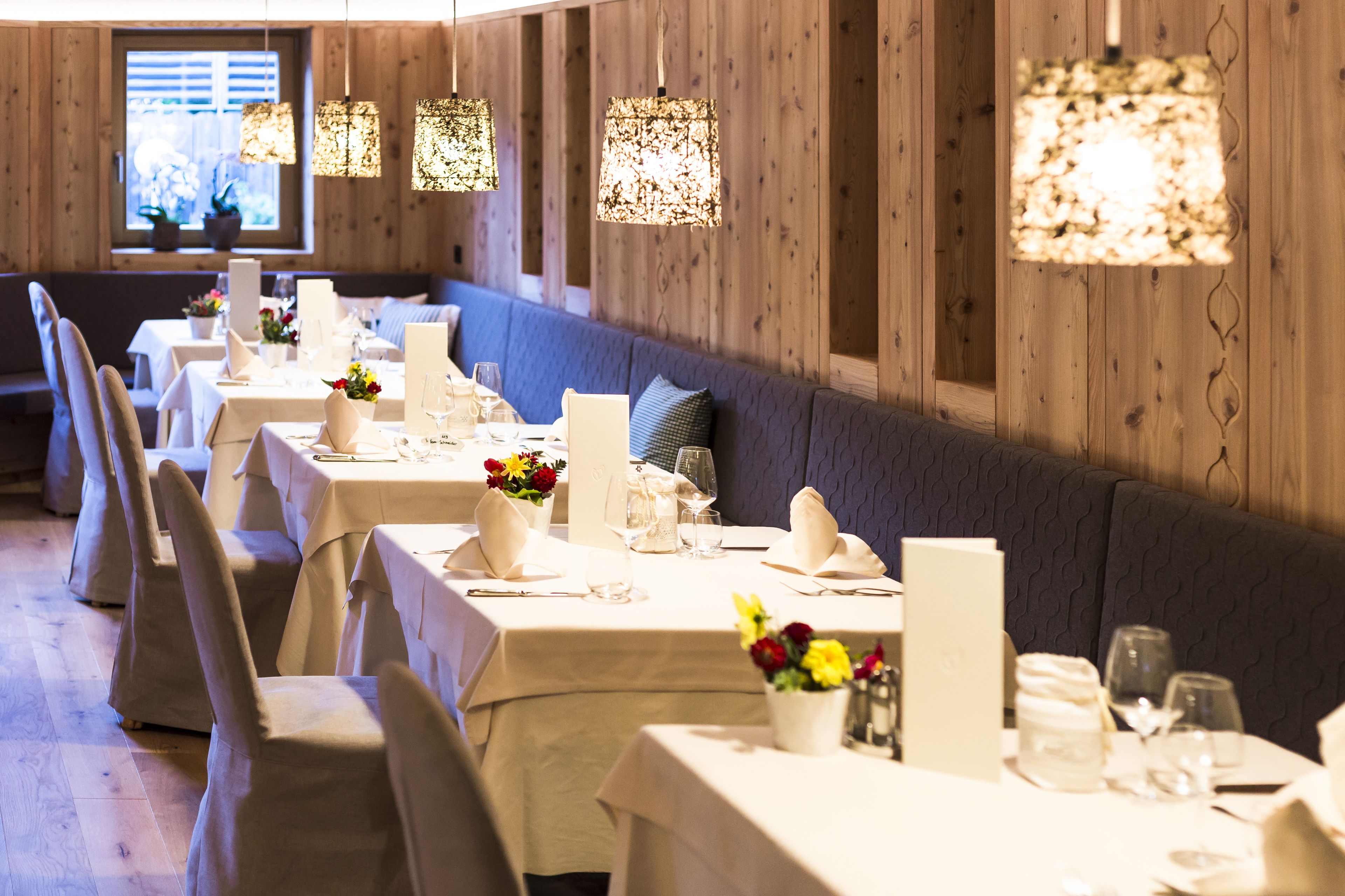 Un restaurante con varias mesas dispuestas para comer, cada una con un jarrón de flores, vasos y cubiertos.
