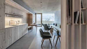 A modern kitchen with wooden cabinets, a central island, and a dining area with chairs and tables. - Hotel Langgenhof (Brunico)