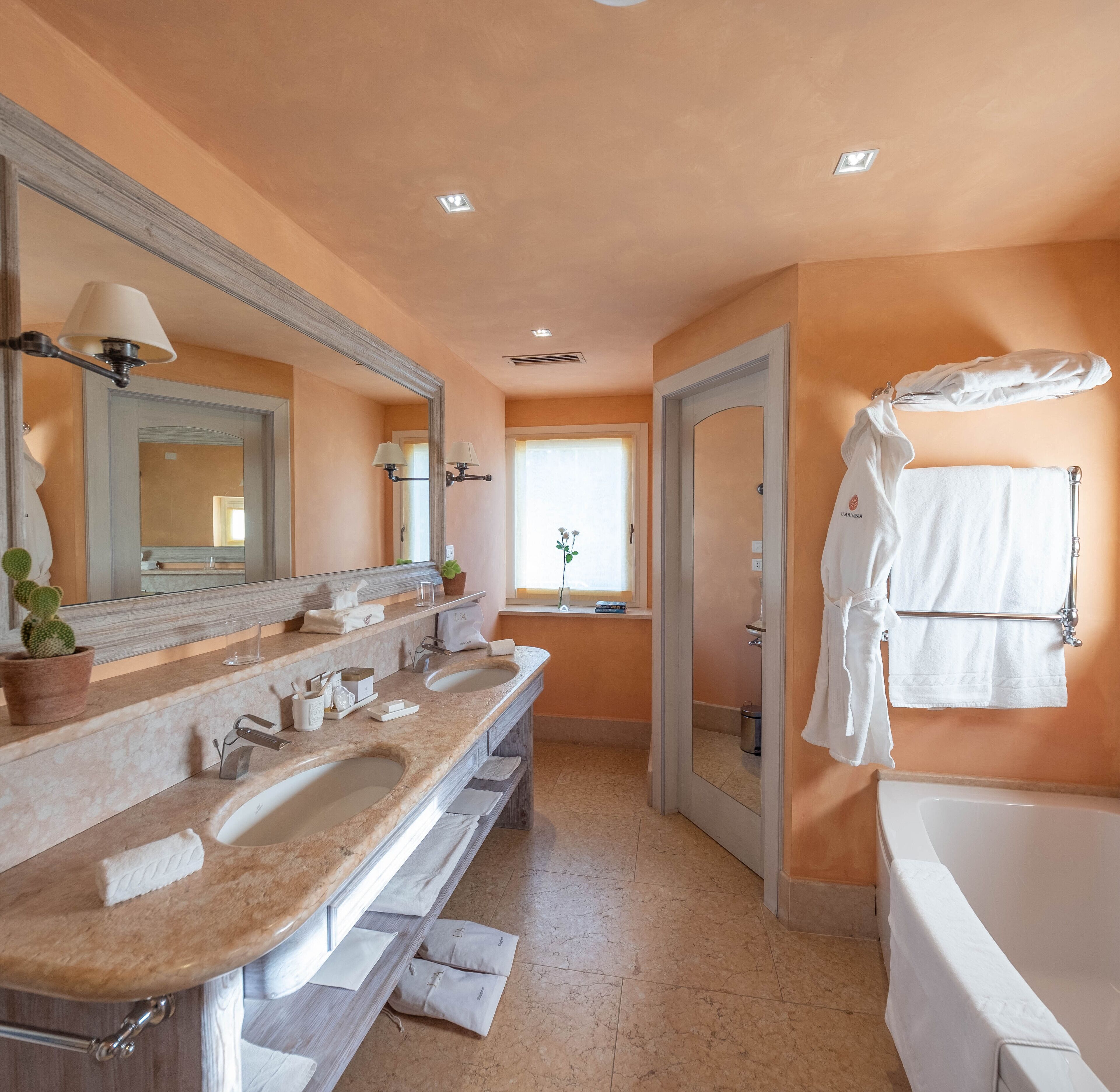 Un baño con tocador doble, un espejo grande, una bañera y un ventanal que permite la entrada de luz natural.