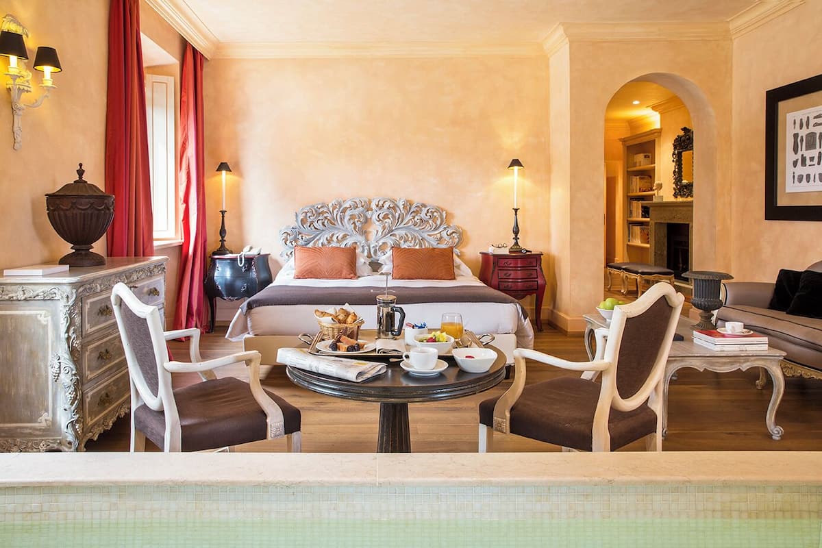 Una habitación de hotel con una cama grande, una mesa de comedor con desayuno, un sofá y vistas al pasillo.