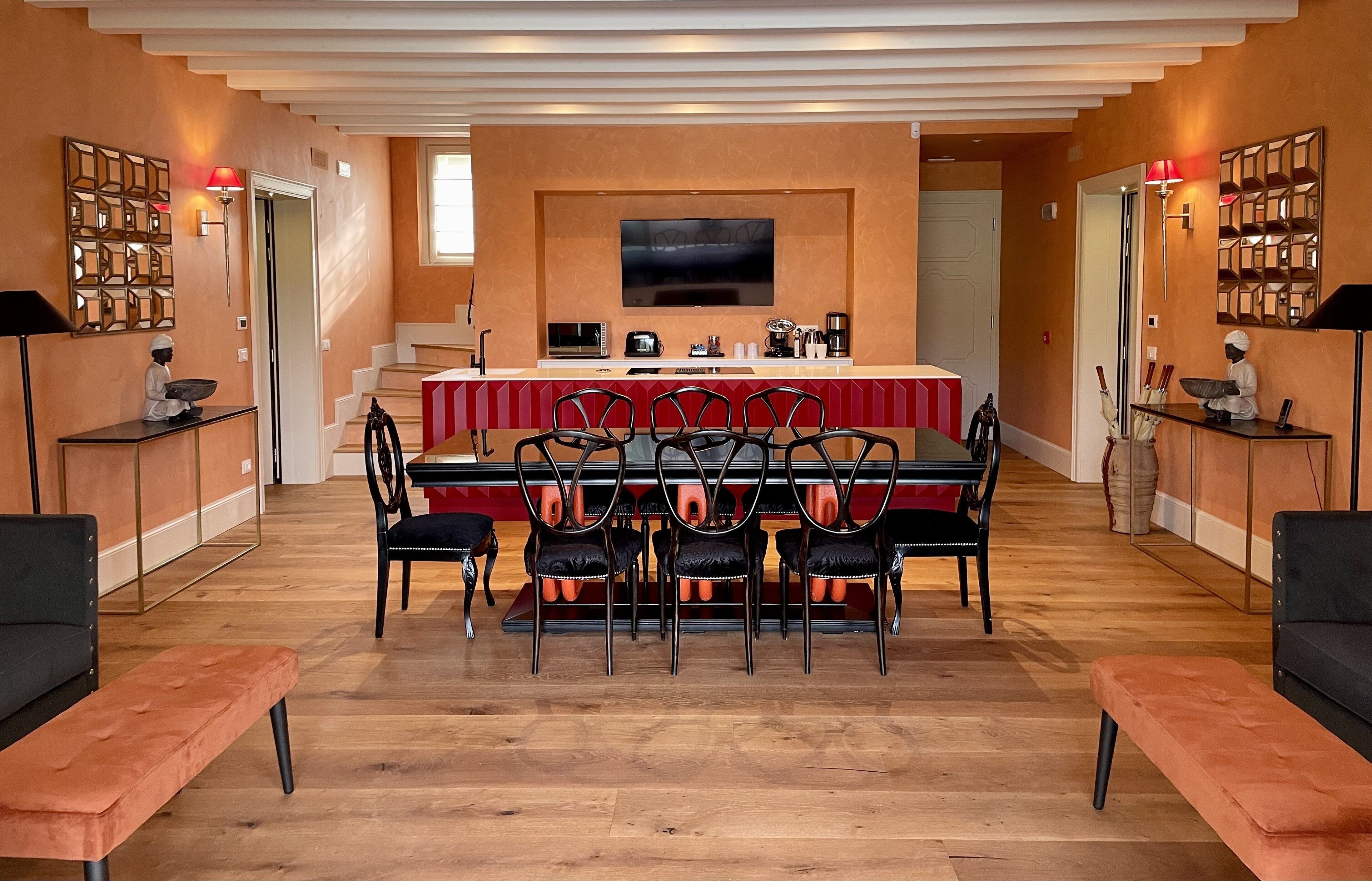 A modern kitchen with a dining area, featuring a large TV, a red and white striped table, and black chairs.