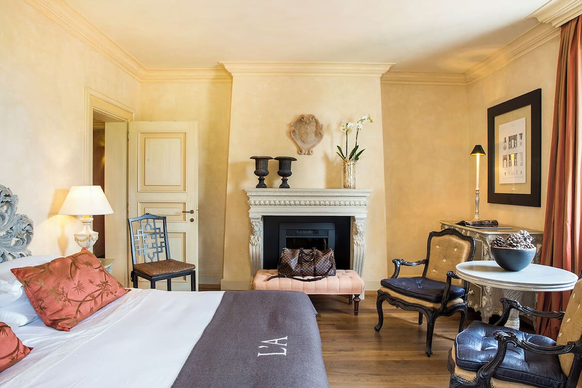 Una habitación de hotel con una cama, una silla, una mesita, una chimenea y una puerta.