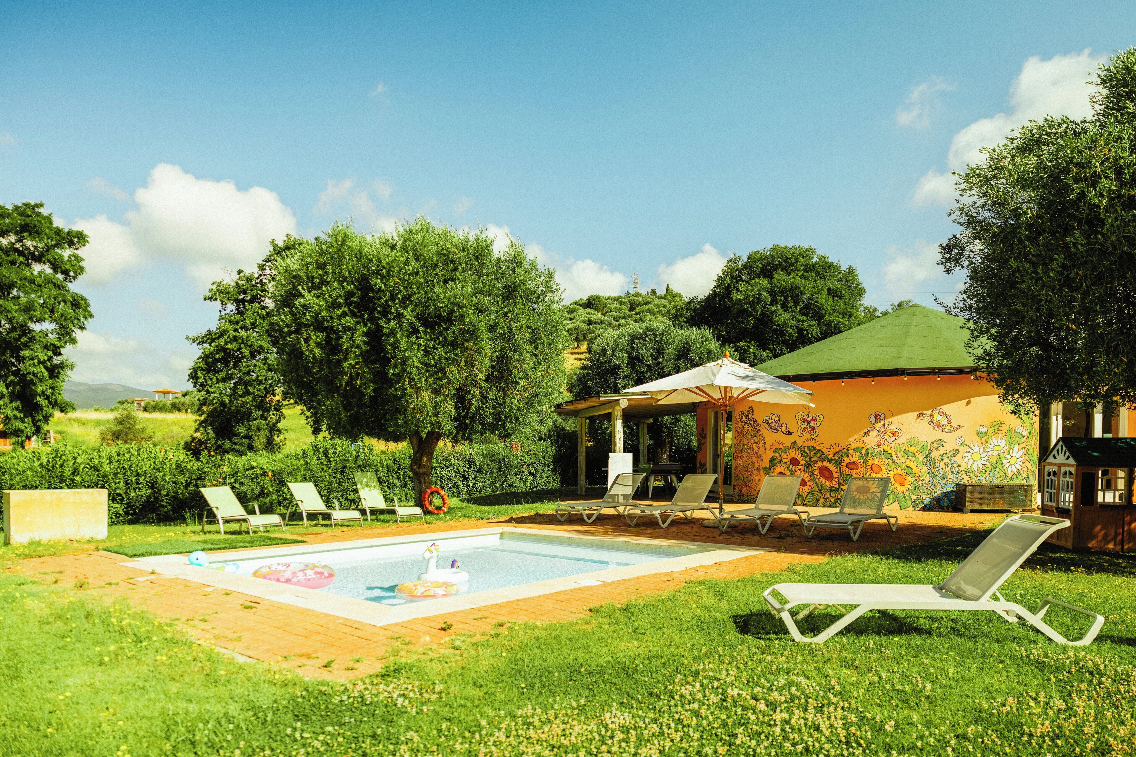 Ett poolområde med solstolar, en liten pool och en pergola med en väggmålning.