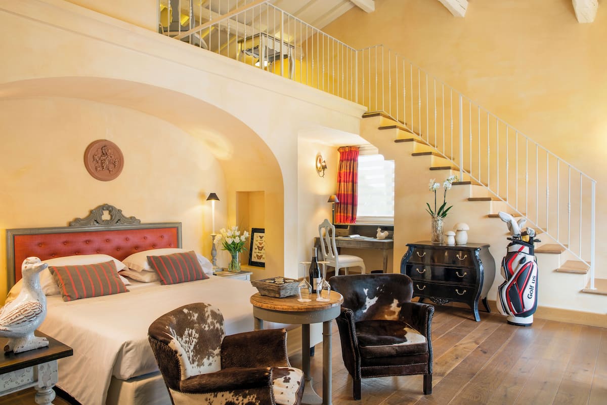 Un espacioso dormitorio con una cama grande, una zona de estar con una silla y una mesa, una escalera y un bolso de golf.