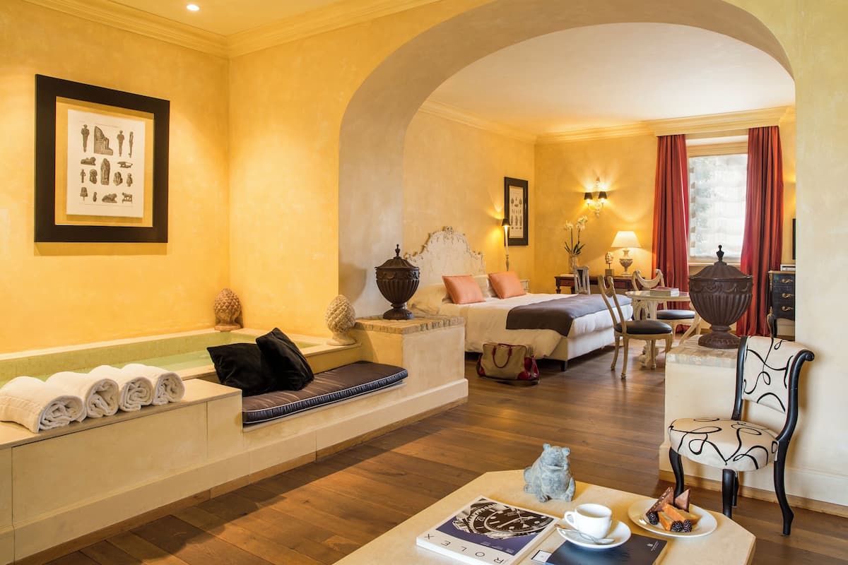 Habitación de hotel con bañera, sofá, mesa de comedor y una cama con mesita de noche.