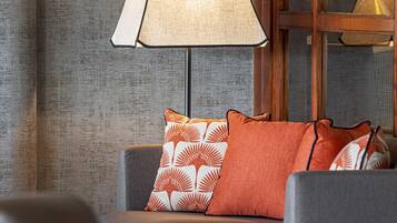 A room with a sofa, patterned cushions, a lamp, and a window with a view.