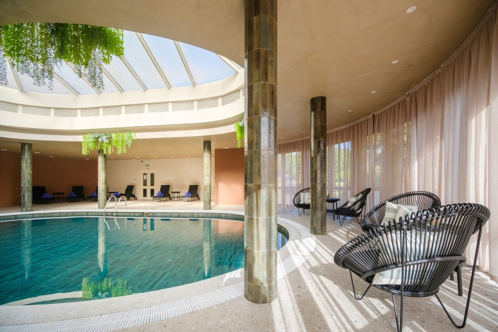 Un espace piscine doté de chaises longues, d’une verrière et d’une structure à colonnes.