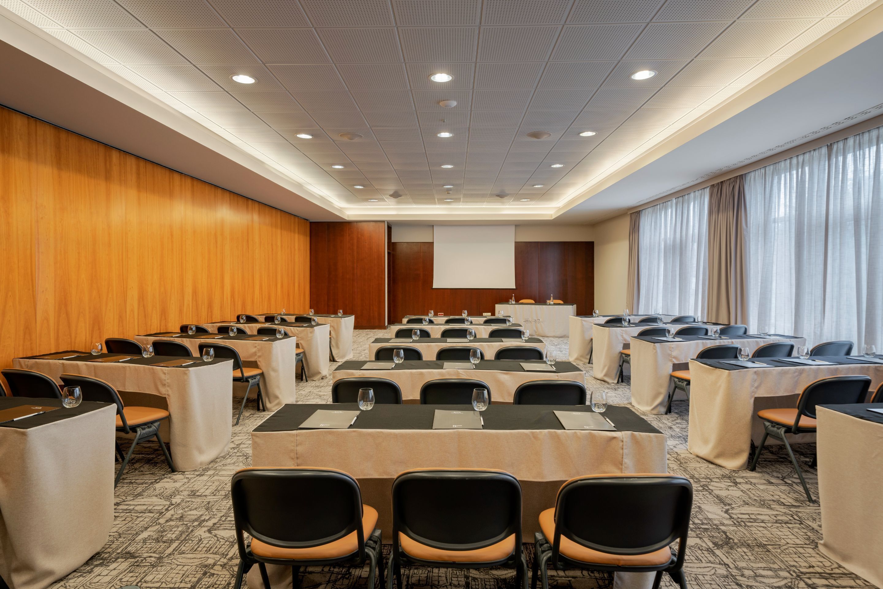 A conference room with tables and chairs, a projector screen, and a large window with curtains.
