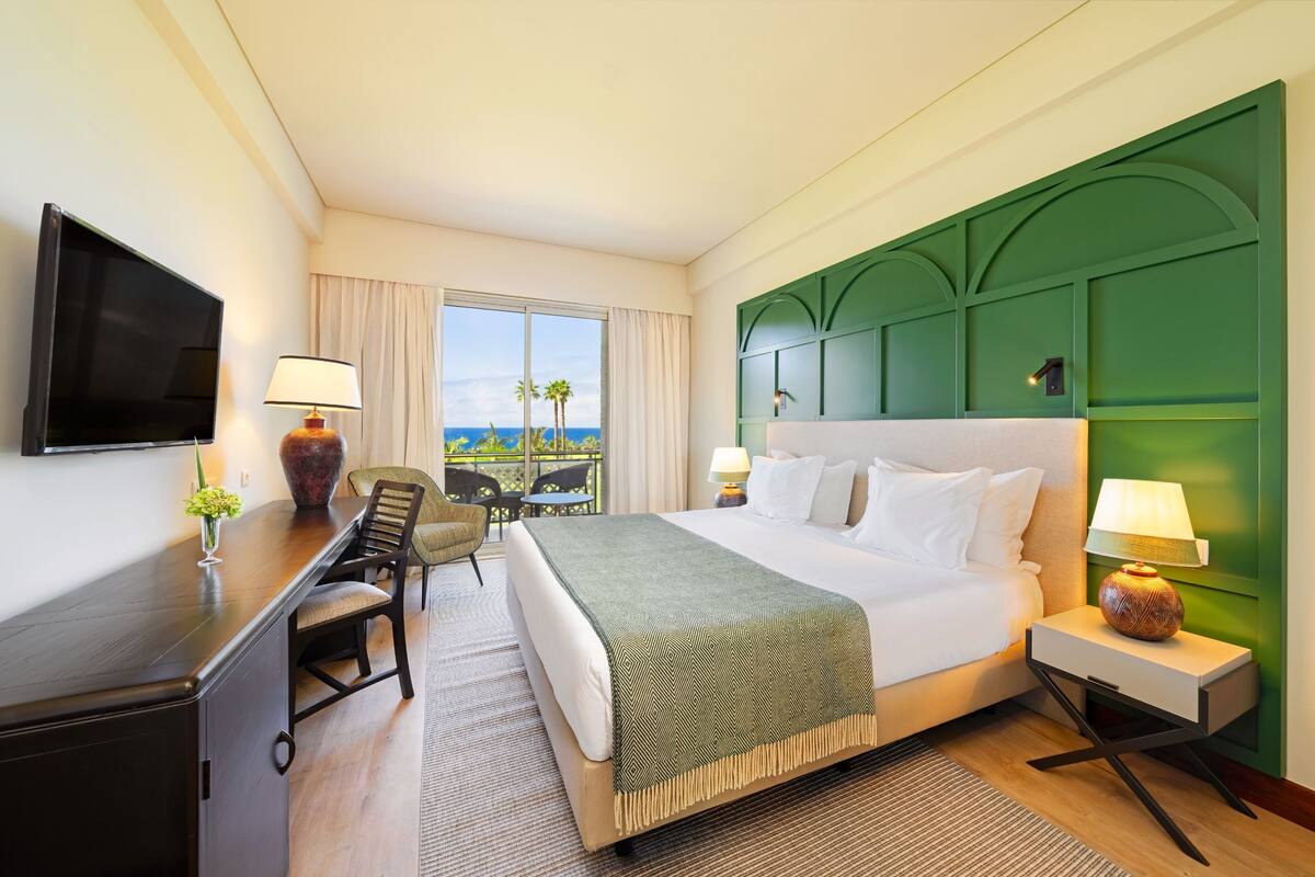 Une chambre d’hôtel comprenant un lit, un bureau, une chaise, une télévision, une fenêtre avec vue et un mur d’accent de couleur verte.