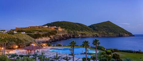 A resort with a swimming pool, palm trees, and a view of the sea.