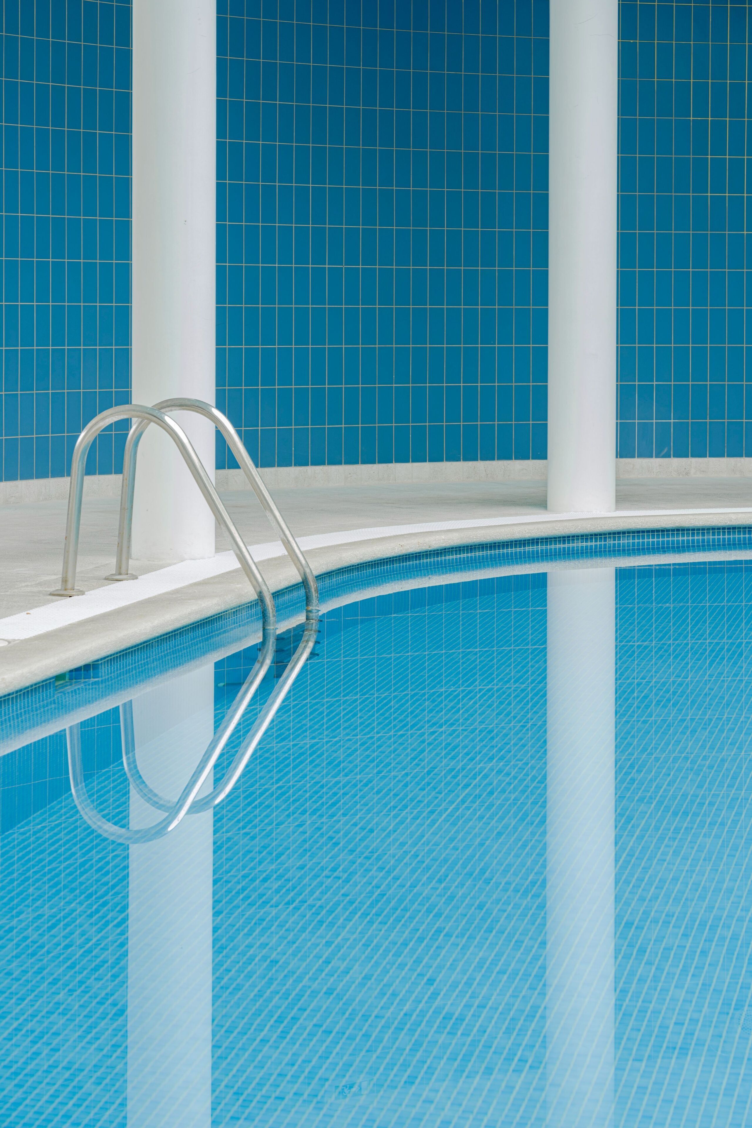 En swimmingpool med metalstige og blå fliserede vægge.