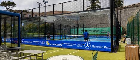 A tennis court with a glass enclosure, seating area, and advertising for Mercedes-Benz.