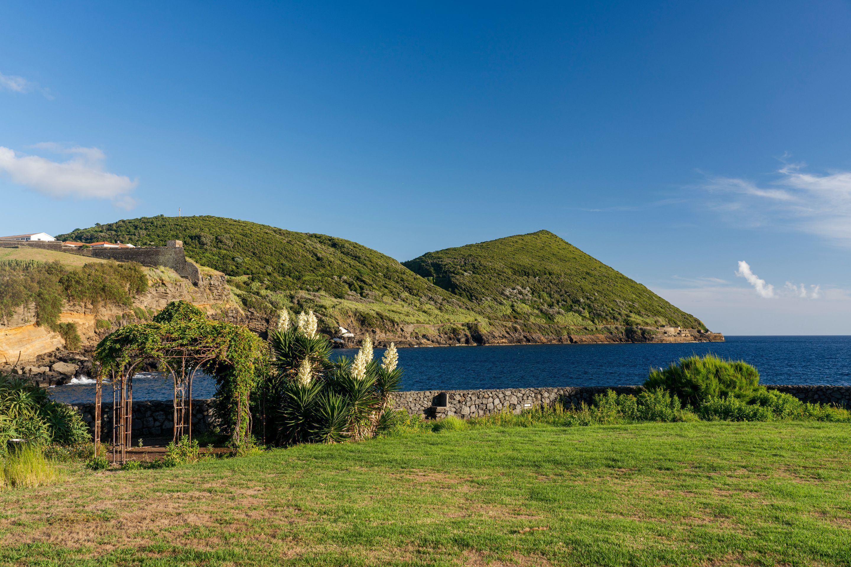 A coastal landscape with a stone wall, grassy area, and a small structure with a roof.