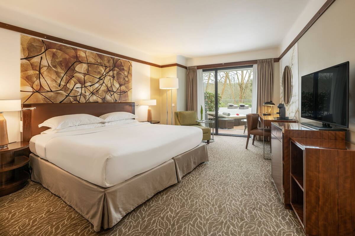 A hotel room with a large bed, a flat-screen TV, a desk, and a view of the outdoors.