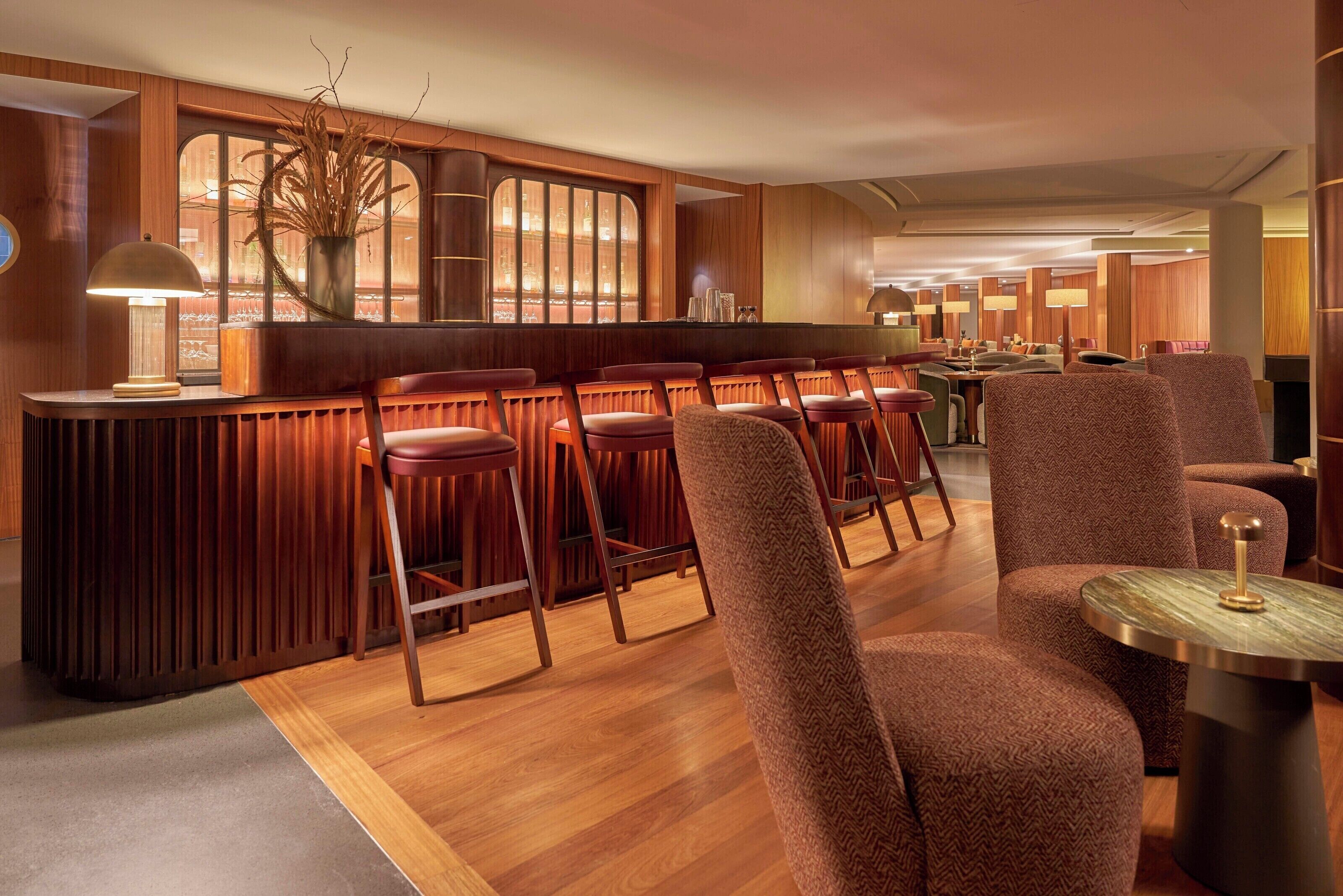 Zona de bar con paneles de madera, taburetes y una barra.