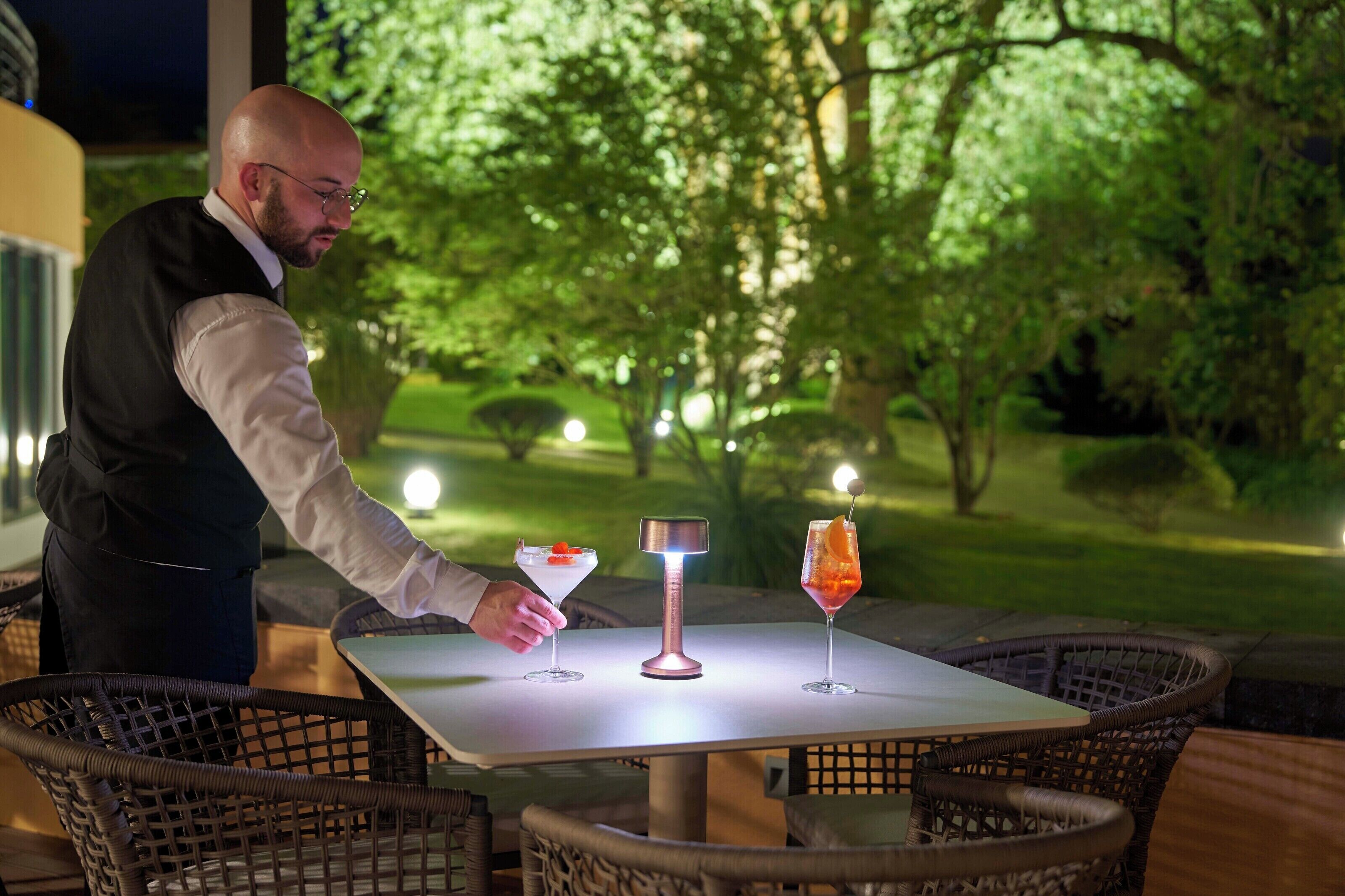 Uma mesa com duas bebidas e uma fonte de luz, rodeada por cadeiras de vime.