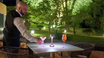 Uma mesa com duas bebidas e uma fonte de luz, rodeada por cadeiras de vime.