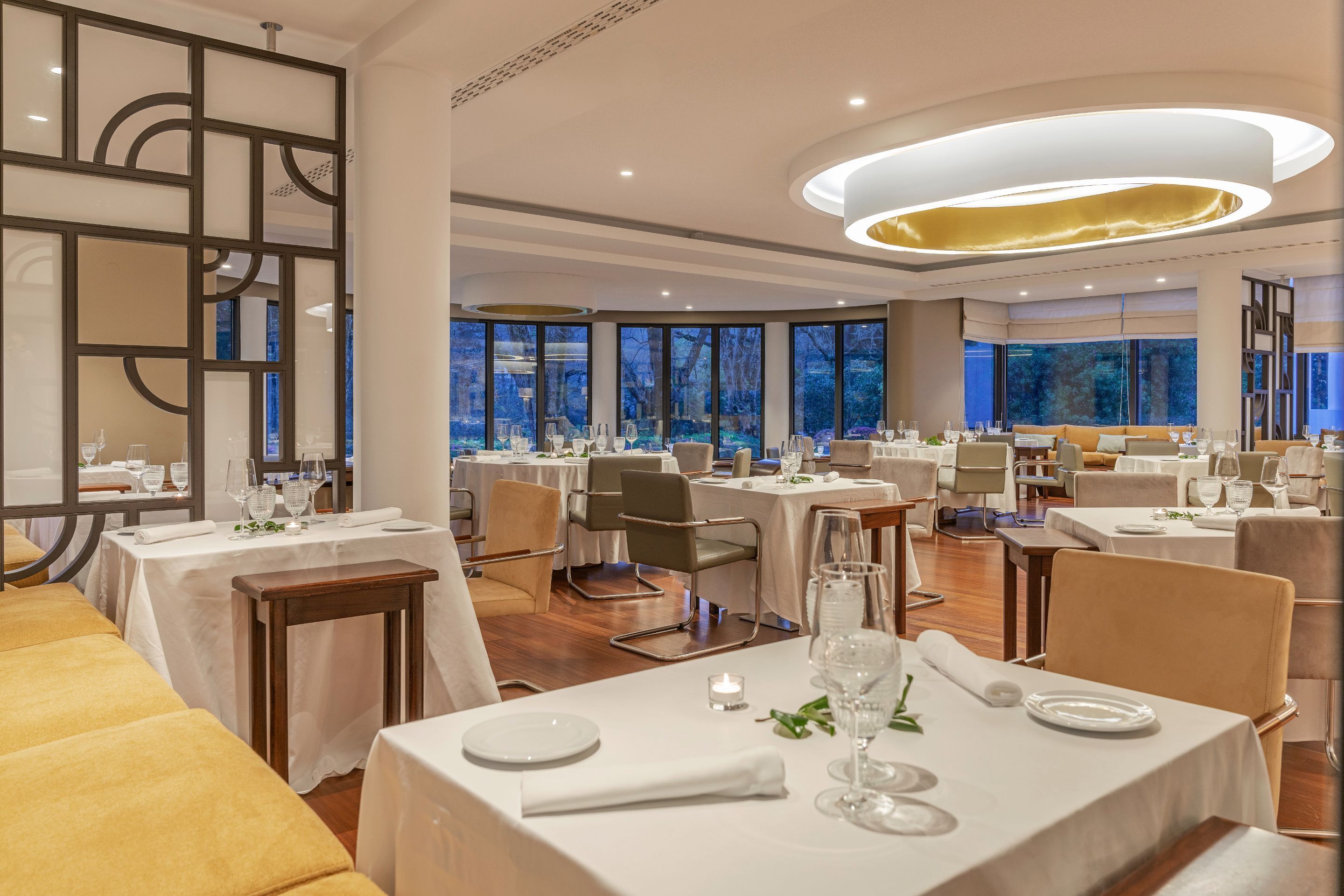 Un comedor moderno con mesas redondas, manteles blancos y vistas al exterior a través de amplias ventanas.